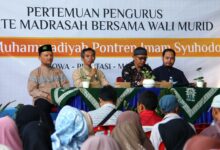 Empat pejabat madrasah duduk di panggung di belakang spanduk untuk rapat wali murid MTs Muhammadiyah Pontren Imam Syuhodo.