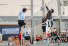 Pemain bola voli UMS melompat smes bola melintasi net di hadapan dua pemain lawan dalam Turnamen Bola Voli UMS Milad ke-68 di GOR FEB.
