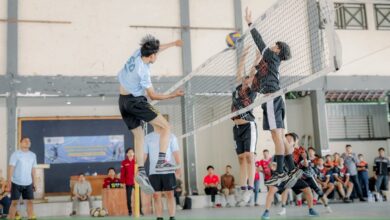 Pemain bola voli UMS melompat smes bola melintasi net di hadapan dua pemain lawan dalam Turnamen Bola Voli UMS Milad ke-68 di GOR FEB.