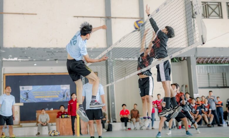Pemain bola voli UMS melompat smes bola melintasi net di hadapan dua pemain lawan dalam Turnamen Bola Voli UMS Milad ke-68 di GOR FEB.