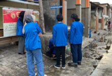 Mahasiswa PPK ORMAWA UNIMUS jas biru memasang plang penunjuk arah Lokasi Desa Wisata Lentera Tambak Lorok Semarang