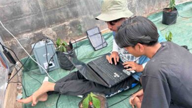 Dua mahasiswa UMS sedang mengonfigurasi perangkat IoT untuk sistem smart farming kopi boyolali di dalam greenhouse Desa Seboto.