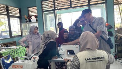 Sekelompok orang sedang mengerumuni sebuah mesin jahit di dalam sebuah ruangan bengkel, mendengarkan penjelasan dari seorang instruktur tentang cara mengoperasikannya dalam rangka pelatihan produksi batik ciprat.