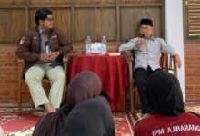 Sastrawan Ahmad Tohari mengenakan kemeja putih dan peci hitam sedang berbicara memegang mikrofon di depan peserta Kelas Literasi IPM Banyumas.