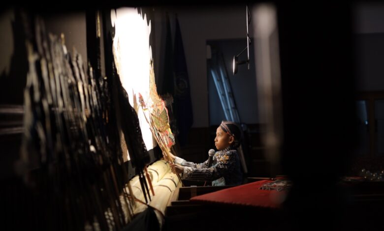 Foto dalang cilik Aditya Ghandi sedang memegang gunungan wayang kulit di depan layar putih bercahaya, dalam rangkaian acara Milad ke-68 FKIP UMS.