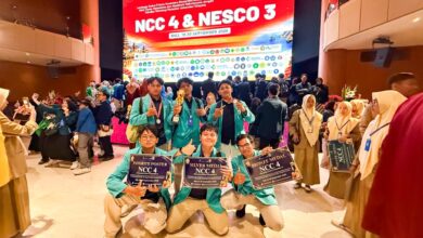 Tim Sang Surya UMS berpose di panggung penghargaan NCC 4 di Bali, memegang tiga sertifikat penghargaan untuk Favorite Poster, Silver Medal, dan Bronze Medal di depan latar panggung merah.