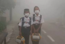Dua anak sekolah dasar memakai masker medis di tengah kepungan kabut asap tebal akibat dampak karhutla pada anak.