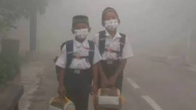 Dua anak sekolah dasar memakai masker medis di tengah kepungan kabut asap tebal akibat dampak karhutla pada anak.