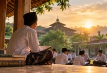 Seorang santri mengenakan peci hitam dan sarung membaca kitab di serambi pesantren, sementara santri lainnya belajar bersama saat matahari terbenam.