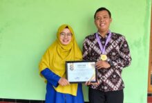 Dosen UNIMUS Prima Trisna Aji memegang piagam penghargaan Juara 1 Lomba Abstrak Nasional dan mengenakan medali bersama seorang wanita.