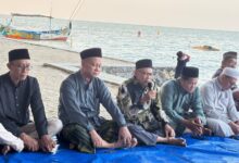 Sejumlah pria berkopiah duduk bersila di tepi pantai mendengarkan penyampaian dalam sebuah acara di pinggir laut.