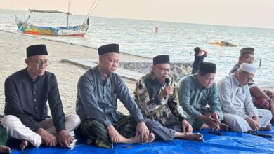 Sejumlah pria berkopiah duduk bersila di tepi pantai mendengarkan penyampaian dalam sebuah acara di pinggir laut.
