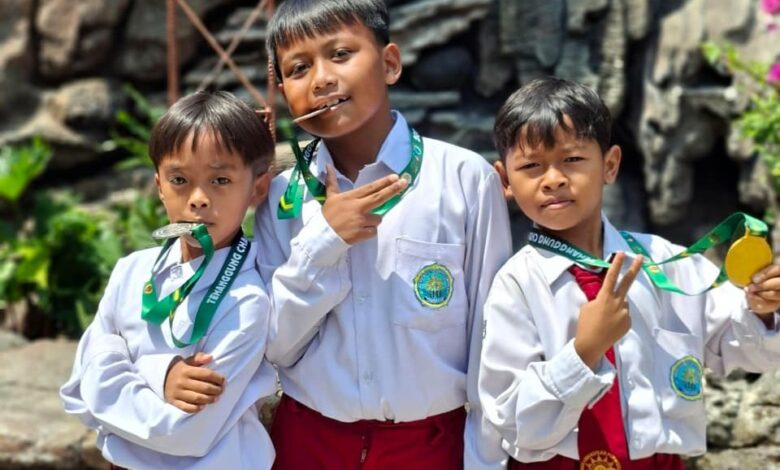 Tiga siswa MI Muhammadiyah Purwodadi mengenakan seragam sekolah sambil memamerkan medali kejuaraan pencak silat Temanggung Open Championship.