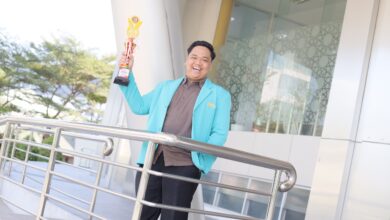 Hian Risnandar, mahasiswa UMS terpilih jadi Pemuda Pelopor Karanganyar, berpose tersenyum sambil mengangkat piala kejuaraan.