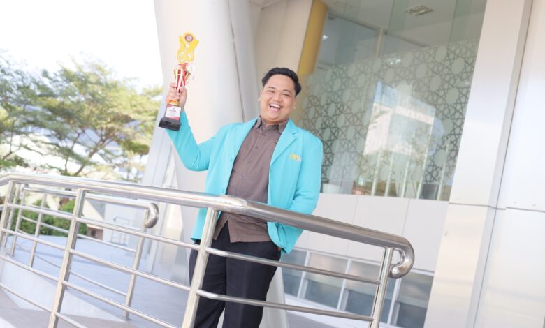 Hian Risnandar, mahasiswa UMS terpilih jadi Pemuda Pelopor Karanganyar, berpose tersenyum sambil mengangkat piala kejuaraan.