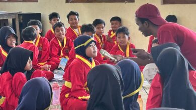 Mahasiswa asing UMS memegang mikrofon dan mengajarkan bahasa Inggris kepada siswa MIM Trangsan berseragam Tapak Suci.