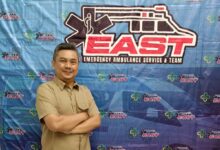 Dosen FIKes UMP Endiyono bersedekap dada di depan latar spanduk pelatihan Emergency Ambulance Service and Team (EAST) RSUD Dr Soetomo Surabaya.
